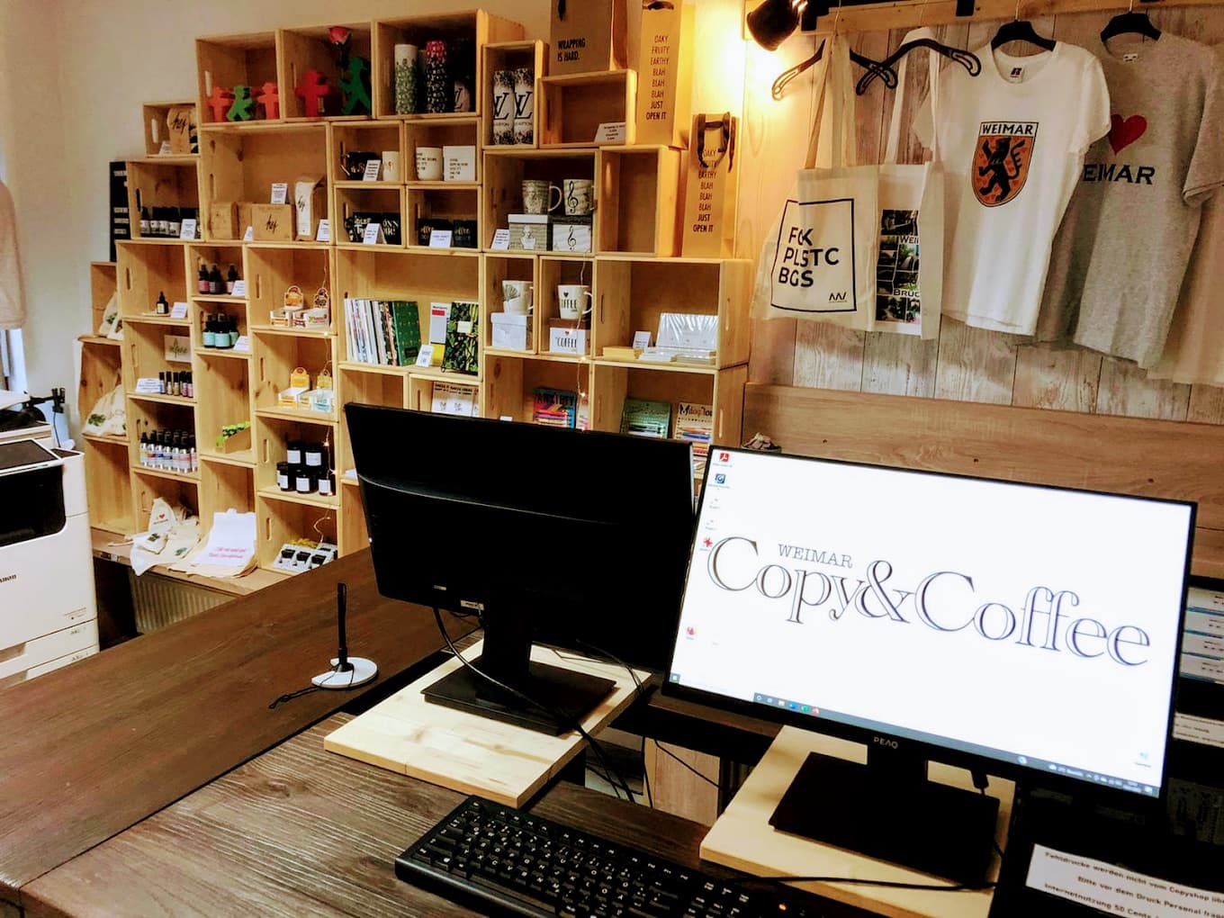 Kunden-Arbeitsplatz im Copyshop: zwei Bildschirme mit Tastatur, dahinter die Regale mit Weimar-Souvenirs