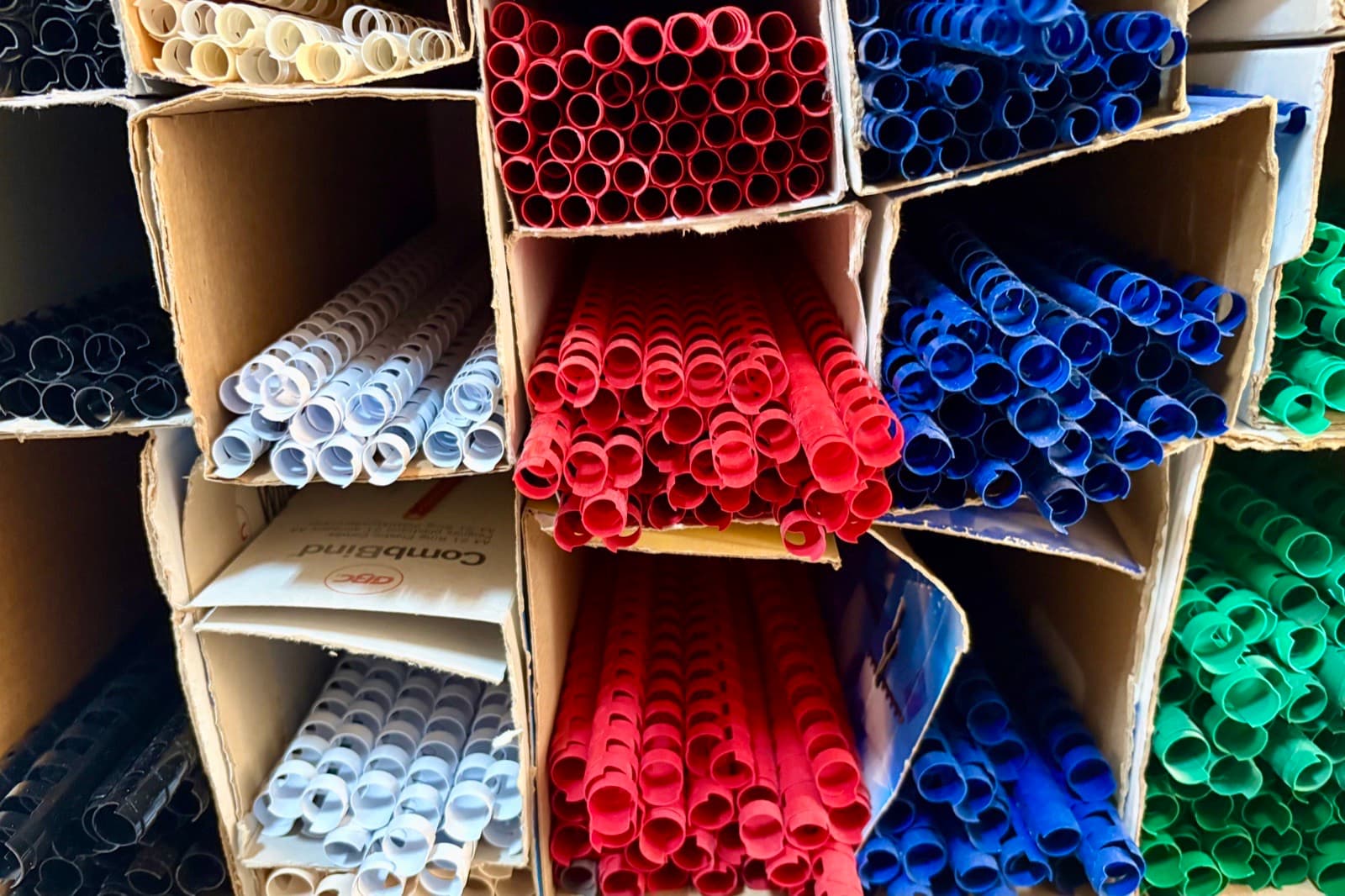 Kisten mit Plastikbinderücken in Rot, Blau, Grün, Weiß, Schwarz und Grau