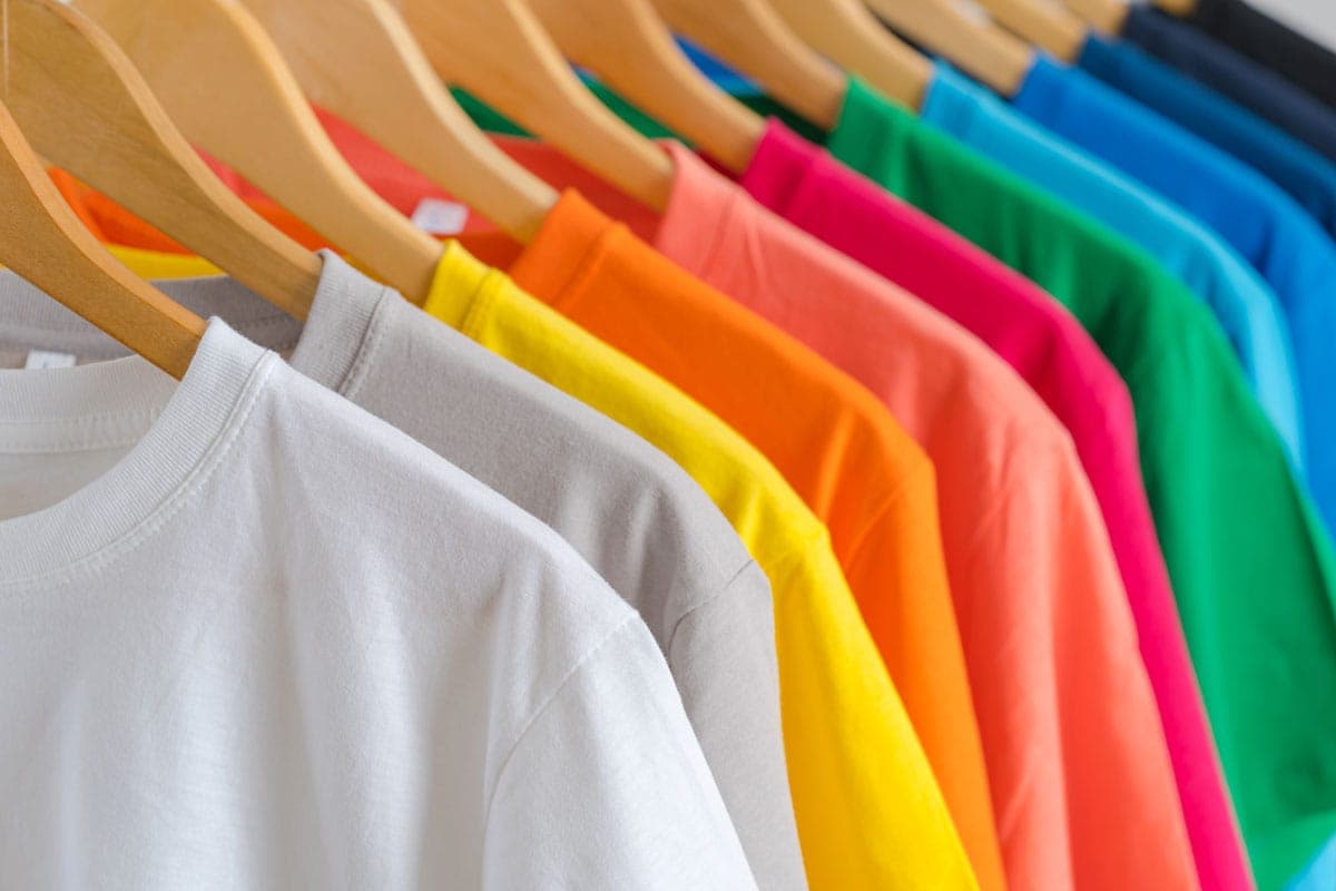 T-Shirts in vielen Farben hängen auf Holzbügeln nebeneinander
